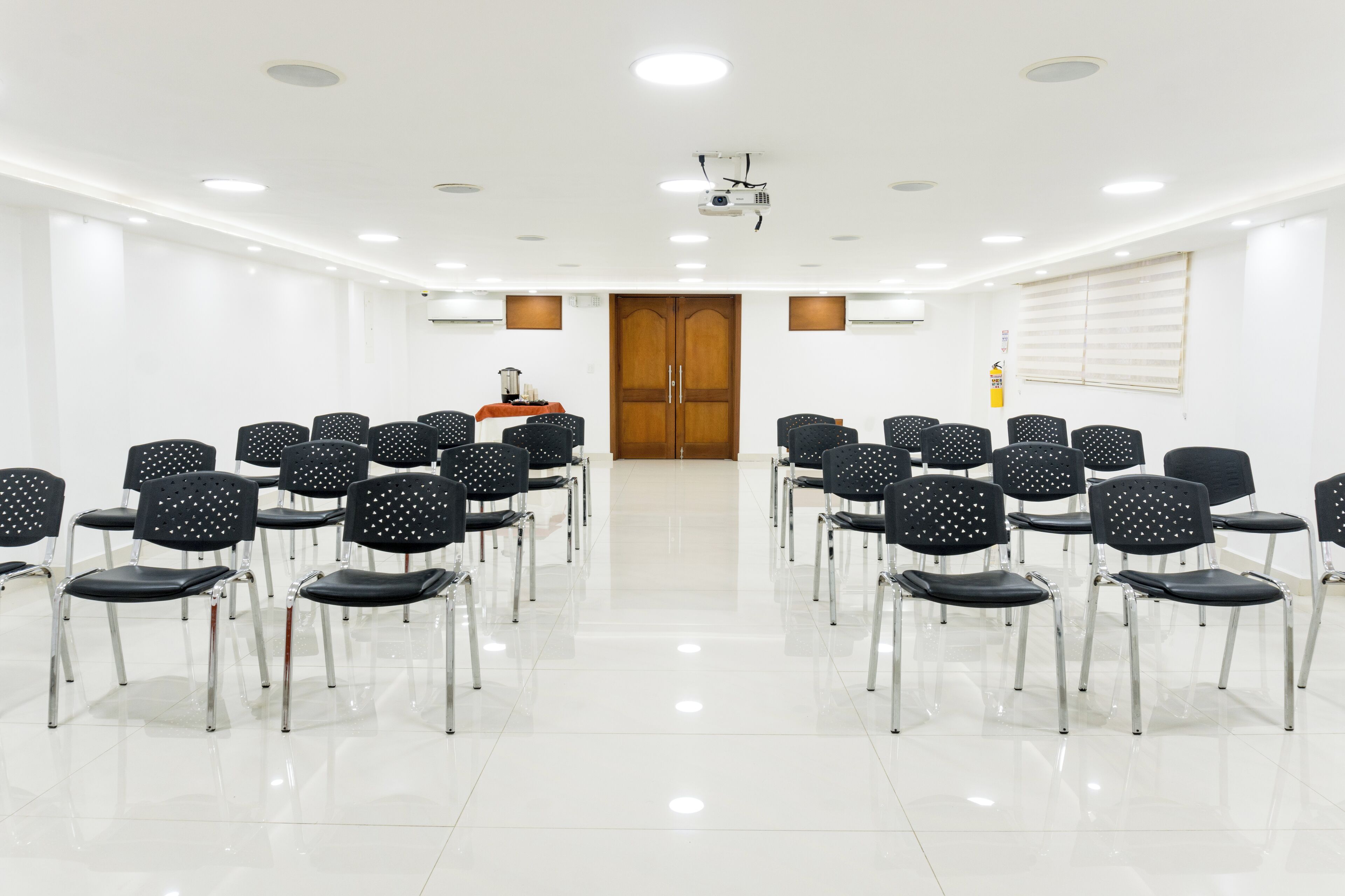 A conference room with rows of black chairs, a projector, and a wooden door.