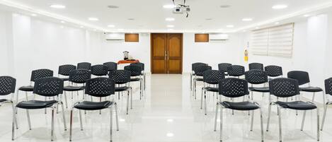 Un salón de conferencias con filas de sillas negras, un proyector y una puerta de madera.