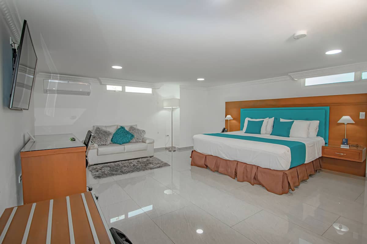 A modern bedroom with a large bed, a white sofa, a wooden nightstand, and a TV mounted on the wall.