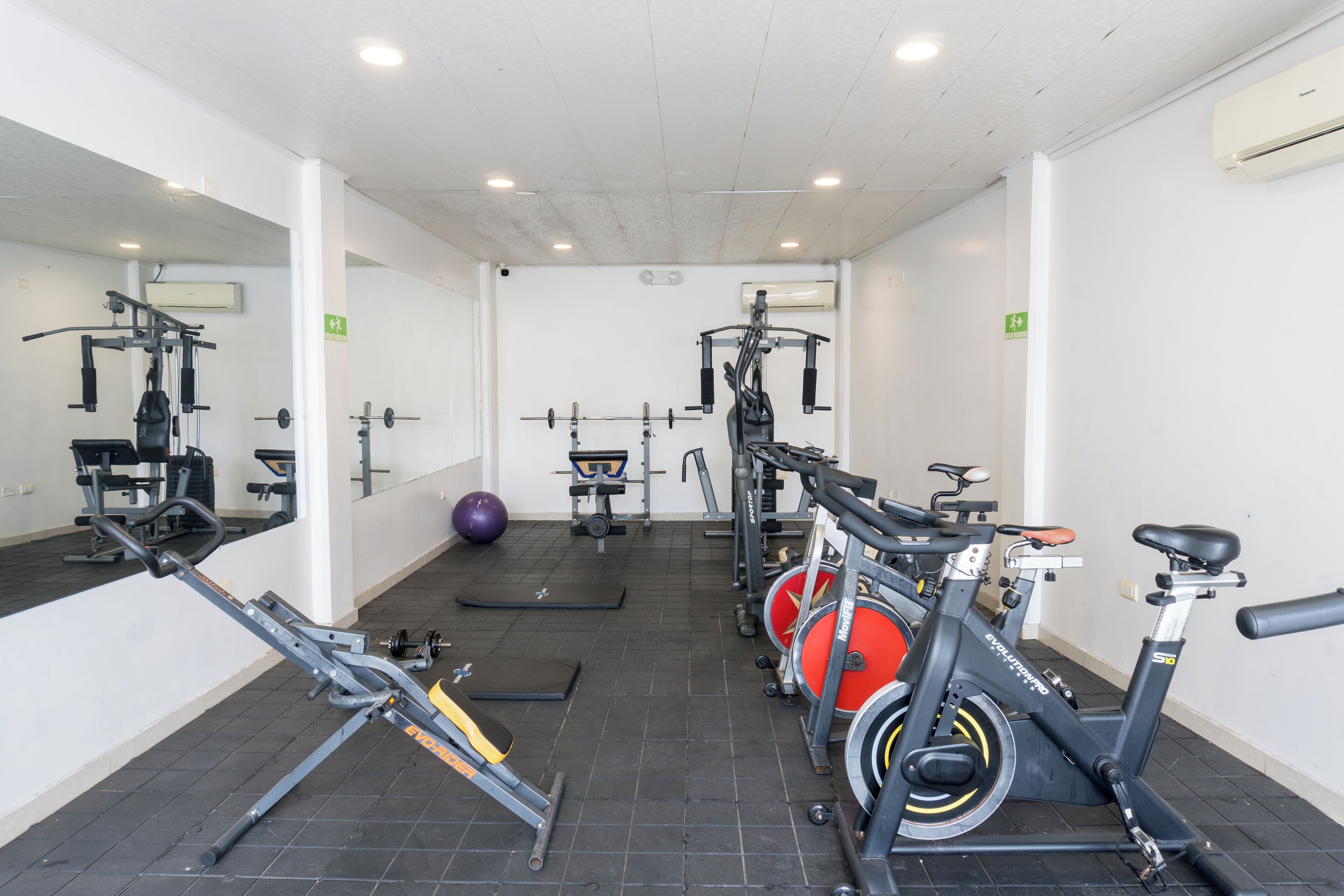 Un gimnasio con equipamiento de ejercicio, un espejo y una colchoneta de goma negra.