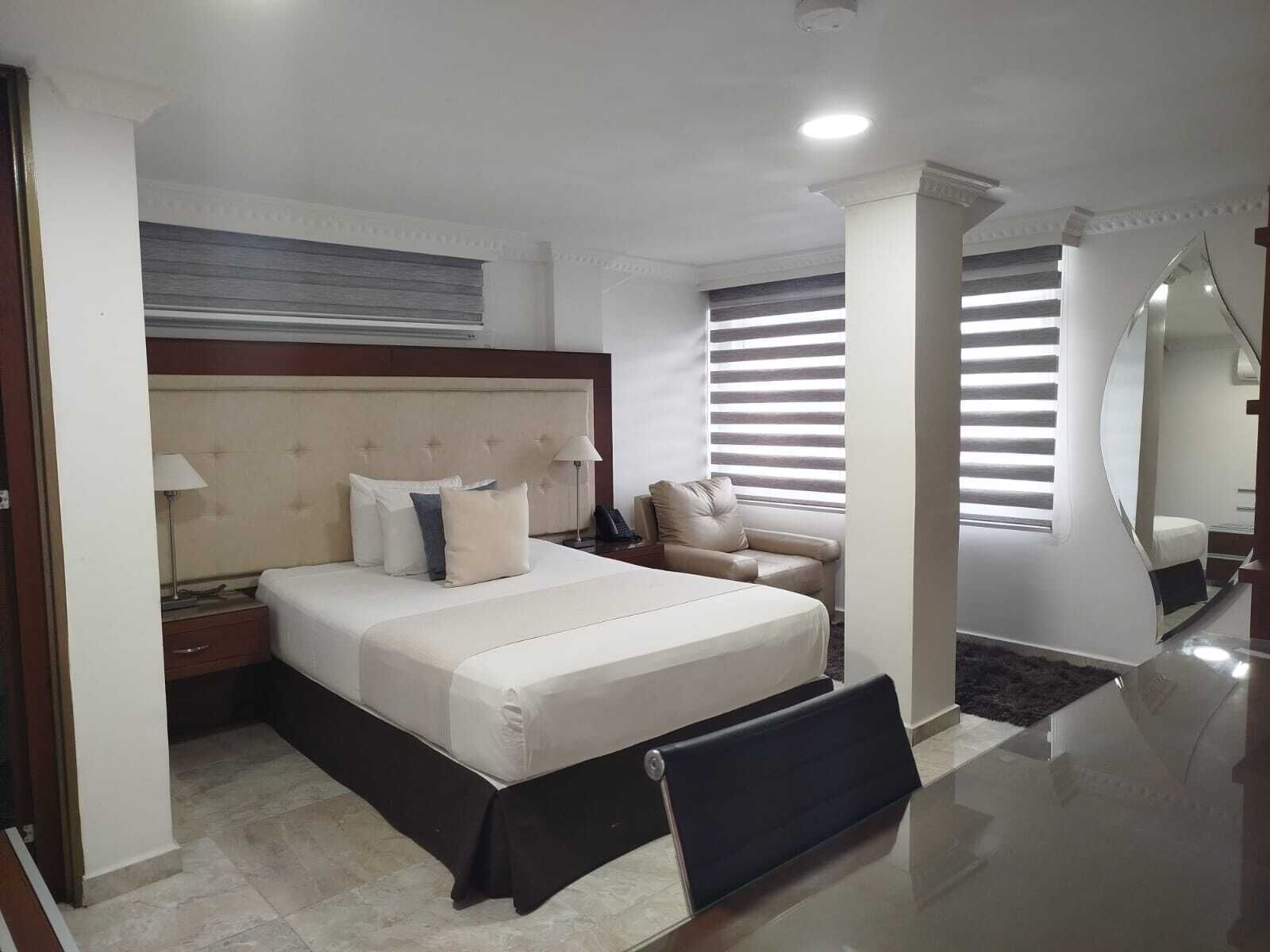 A hotel room with a large bed, a nightstand, a chair, a desk, and a mirror.