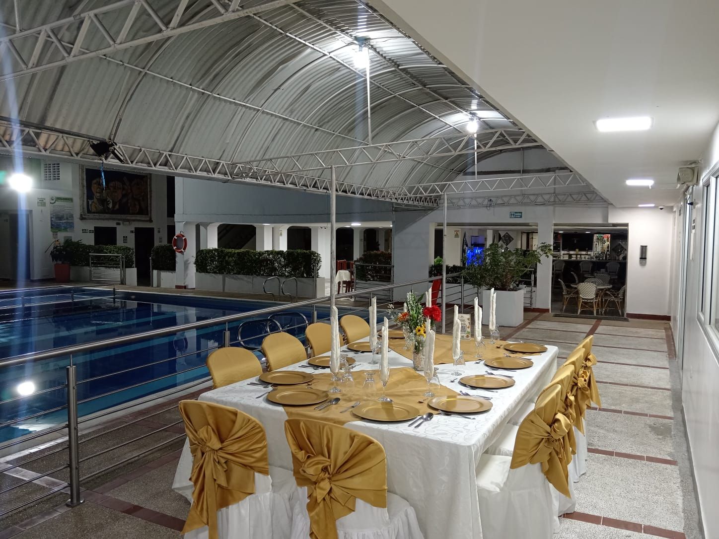 Een binnensaal ingericht als feestzaal met een zwembad, gedekte tafels en een hoge plafond.