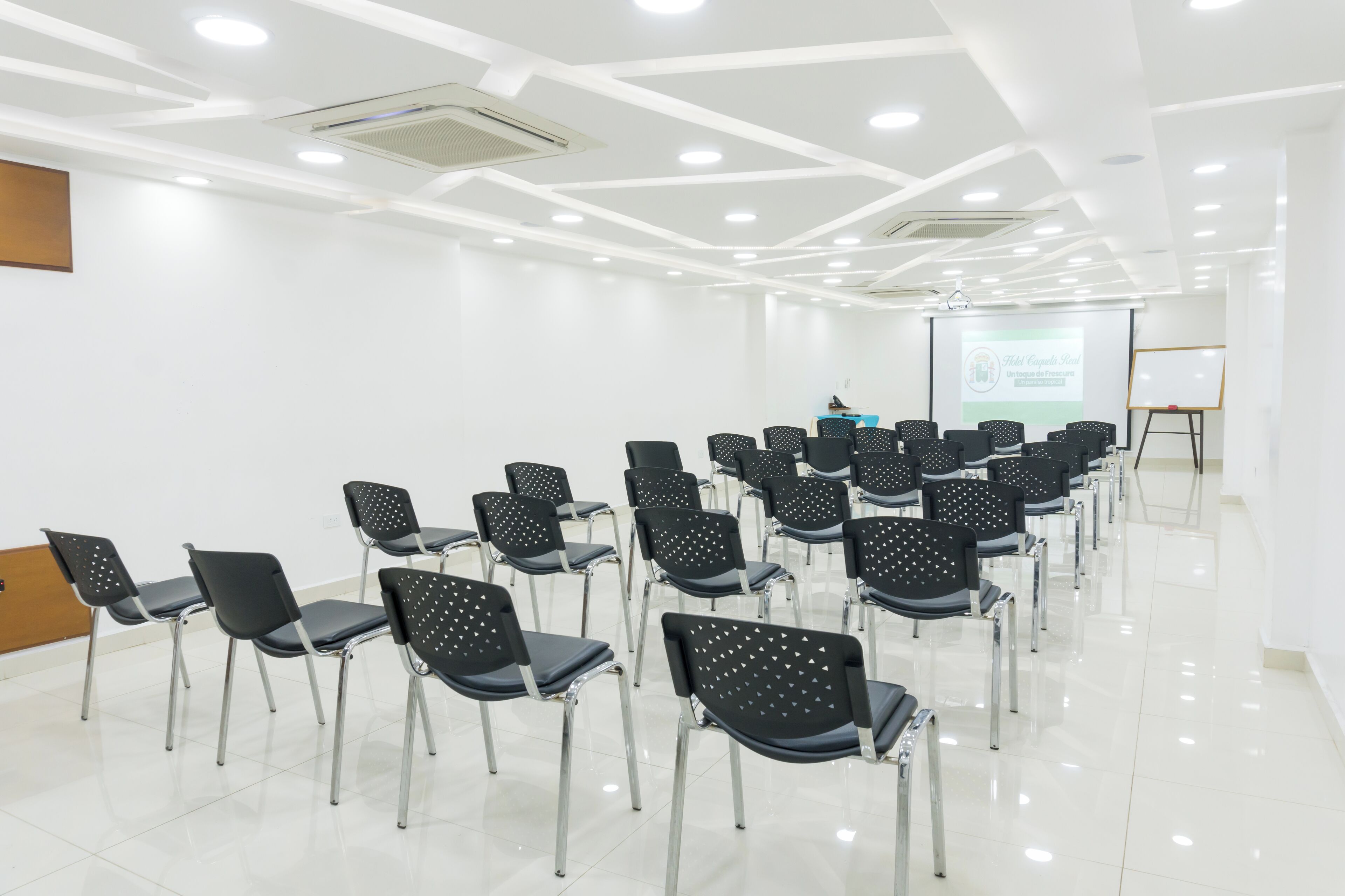 A conference room with rows of black chairs, a whiteboard, and a presentation screen.