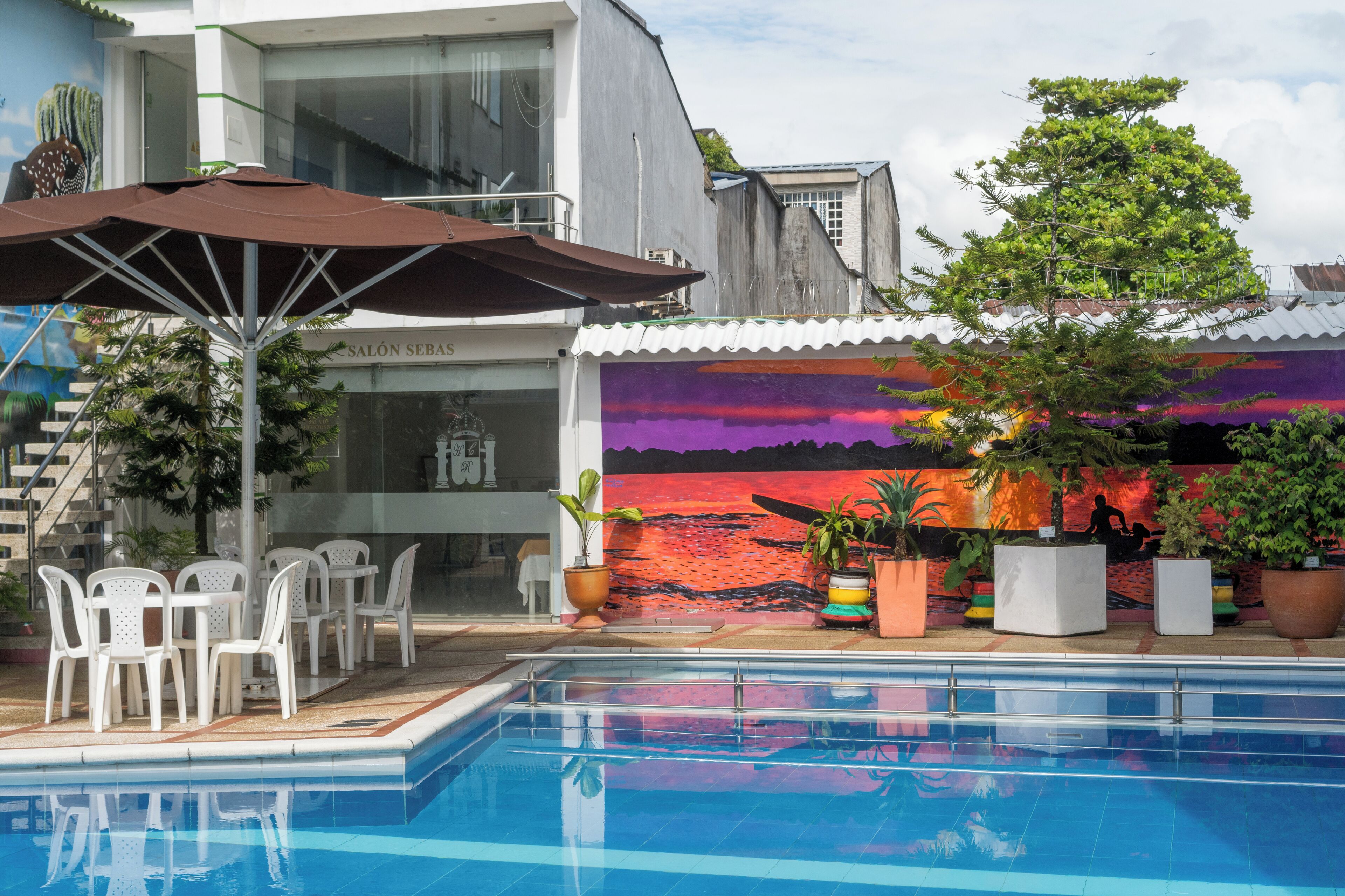 A swimming pool with a mural, outdoor seating, and potted plants.