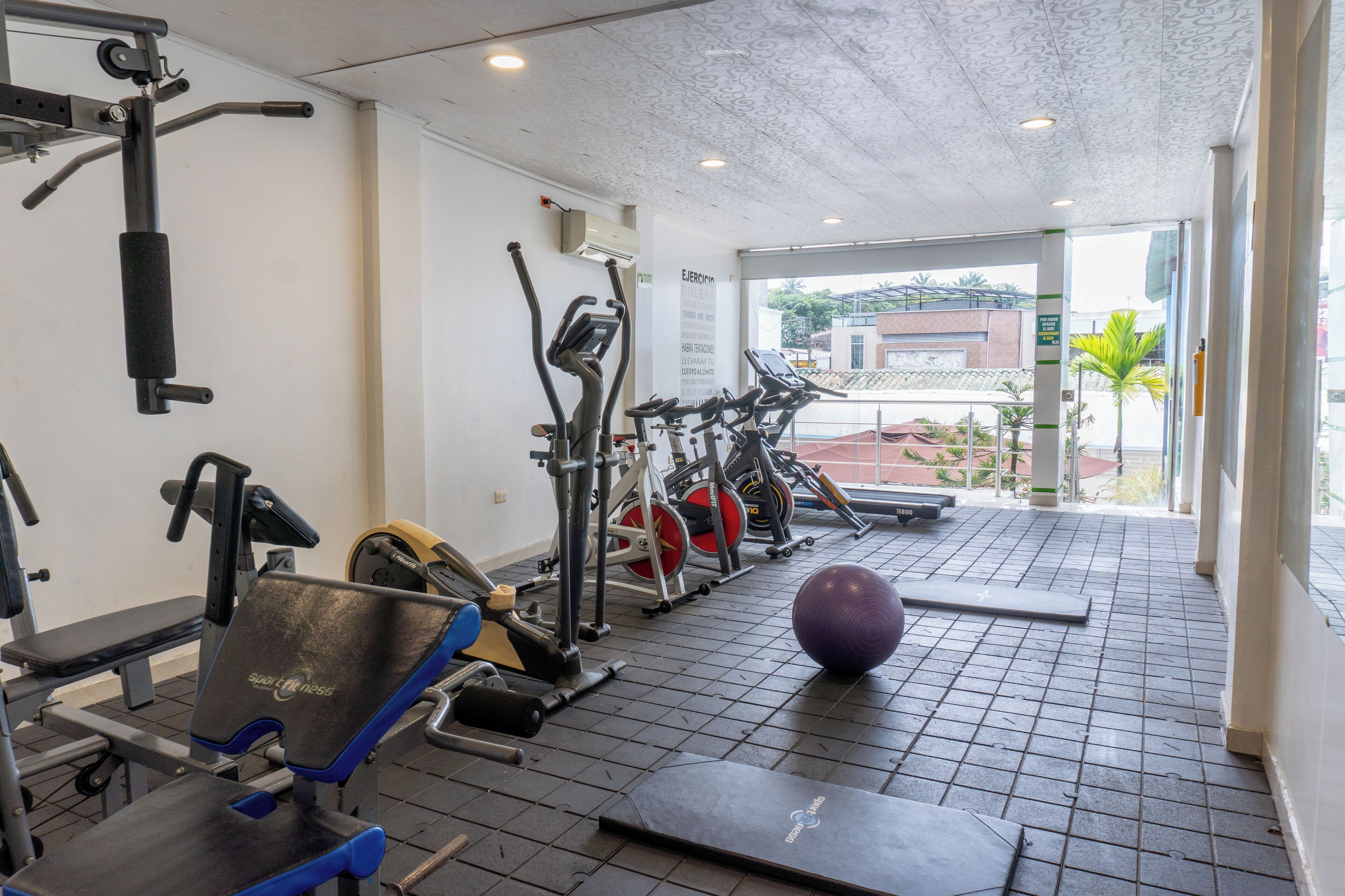 A gym with exercise equipment, a bench, and a large window.