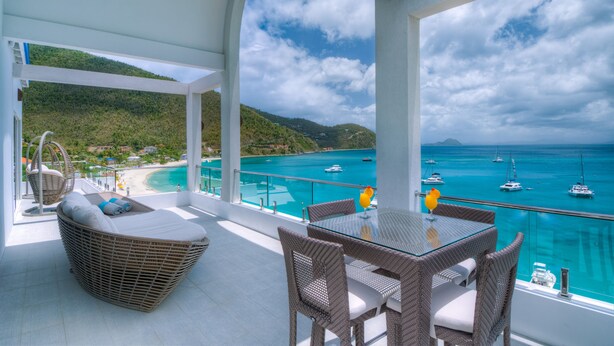 A balcony with wicker furniture, a glass table, and a view of turquoise waters and boats. - Cane Garden Bay Beach Hotel (Cane Garden Bay)