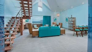 A spacious living area with a staircase, a sofa, a dining table with chairs, and a view of the sea. - Cane Garden Bay Beach Hotel (Cane Garden Bay)