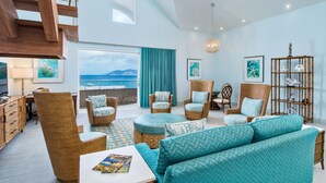 A spacious living room with wicker furniture, a large window overlooking the sea, and a ceiling with wooden beams. - Cane Garden Bay Beach Hotel (Cane Garden Bay)