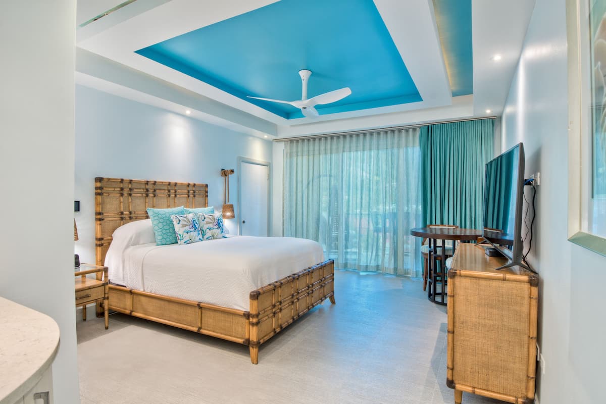 A modern bedroom with a large bed, a ceiling fan, a TV, and a dining area.