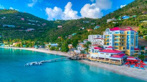 A coastal hotel with multiple floors, a pier extending into the water, and a beach area with umbrellas. - Cane Garden Bay Beach Hotel (Cane Garden Bay)
