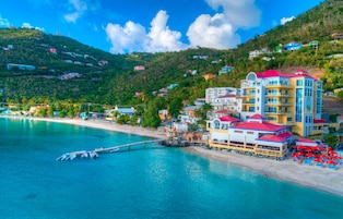 Un hotel costero con varios pisos, un muelle que se adentra en el agua y una zona de playa con sombrillas.