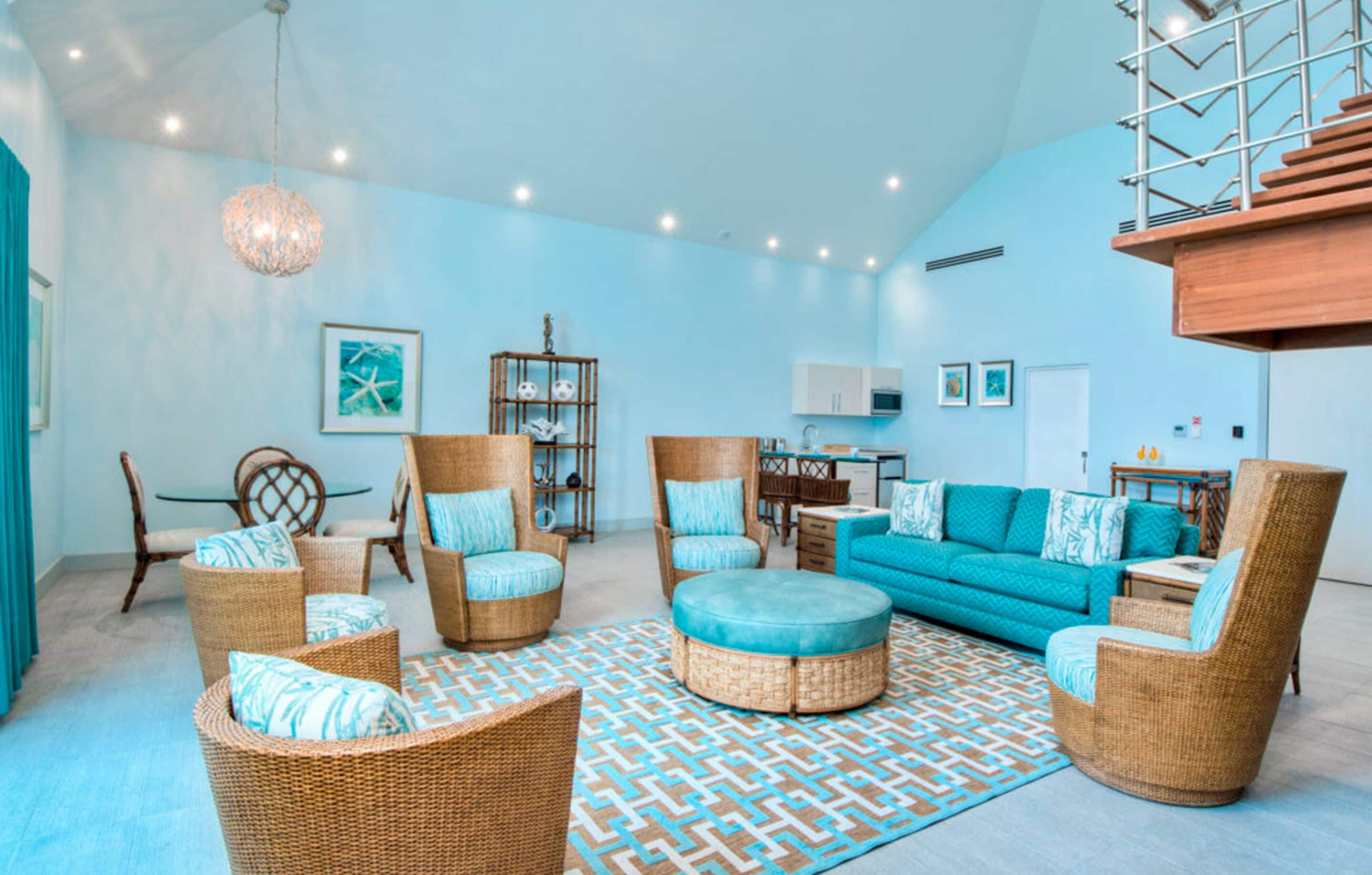 A spacious living room with wicker furniture, a teal sofa, and a patterned rug.