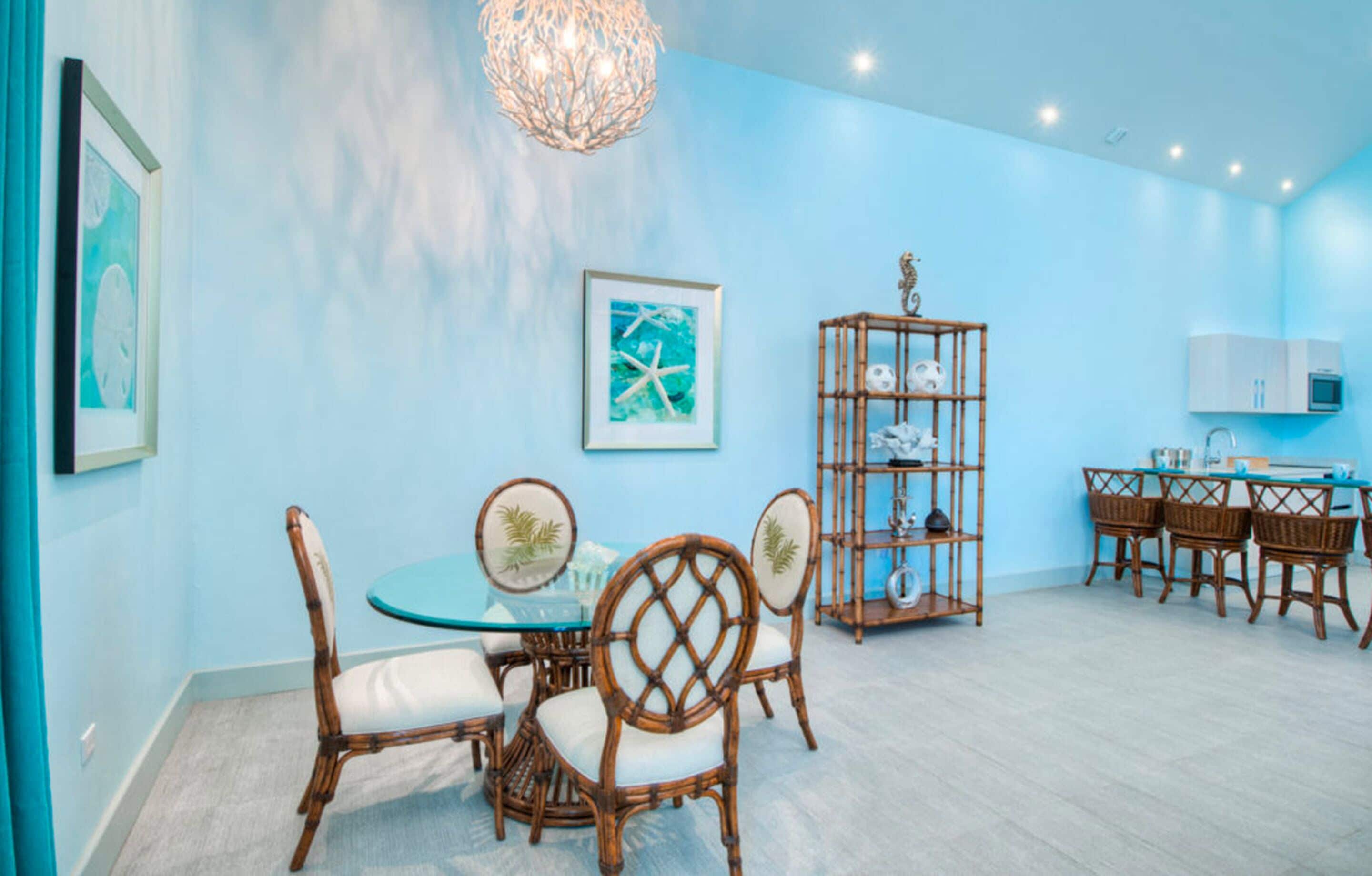 Een eethoek met een ronde glazen tafel, rieten stoelen, een decoratieve wandplank en een blauwe muur.