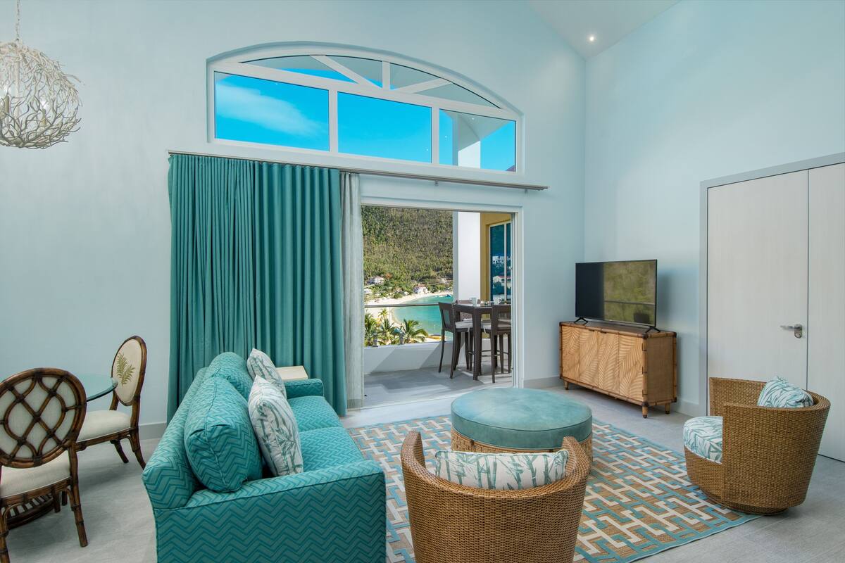 A modern living room with a sofa, ottoman, wicker chairs, a television, and a view of a balcony.