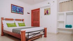 Ein ordentlich eingerichtetes Schlafzimmer mit einem hölzernen Bett, grünen Kissen, einer weißen Wand, einem Gemälde und einer Tür.