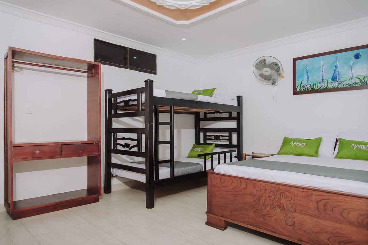 Ein Zimmer mit Etagenbett, Schreibtisch, Stuhl, Bett, Ventilator und einem Bild an der Wand.