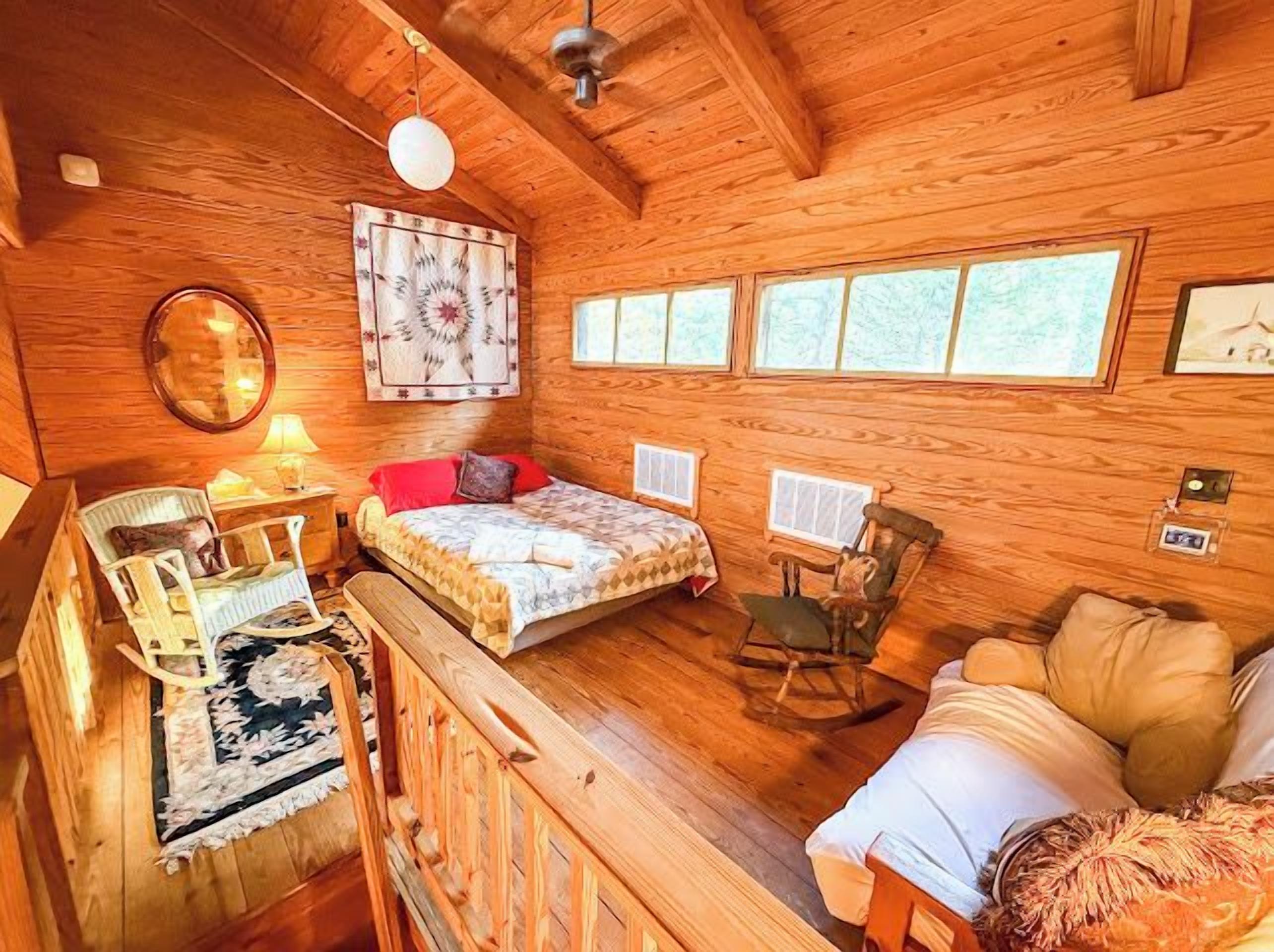 A cozy cabin interior with a bed, a chair, a small table, and a window.