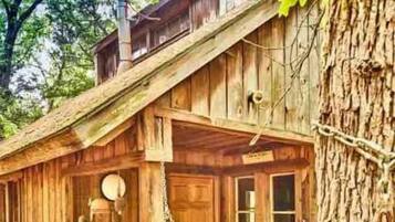 A rustic wooden cabin with a porch, a swing, and a large tree trunk.