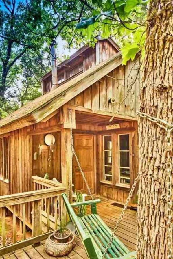 A rustic wooden cabin with a porch, a swing, and a large tree trunk.