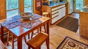 Une cabane en bois comprenant un coin repas, une cuisine et de grandes fenêtres.