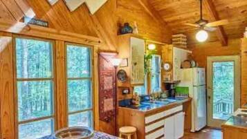 Une cabane en bois comprenant un coin repas, une cuisine et de grandes fenêtres.