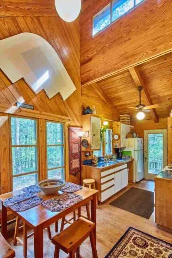 Une cabane en bois comprenant un coin repas, une cuisine et de grandes fenêtres.