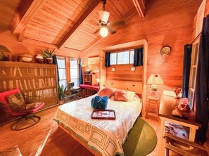 Une chambre confortable, aménagée dans une cabane en bois, avec un lit, une table de chevet, une lampe et une vue sur l’extérieur.