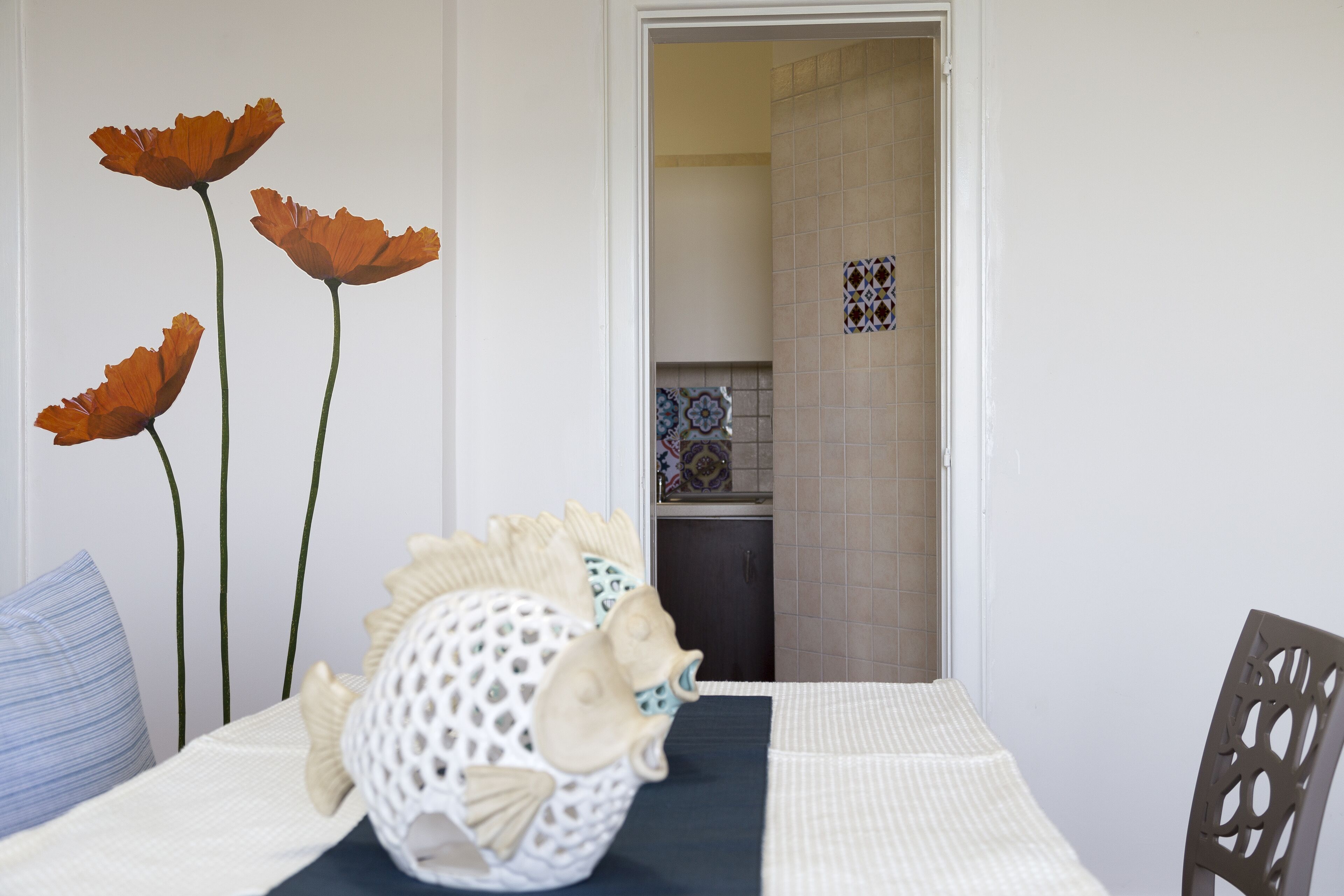 A dining area with a table set for two, a decorative fish sculpture, and a view into the kitchen.