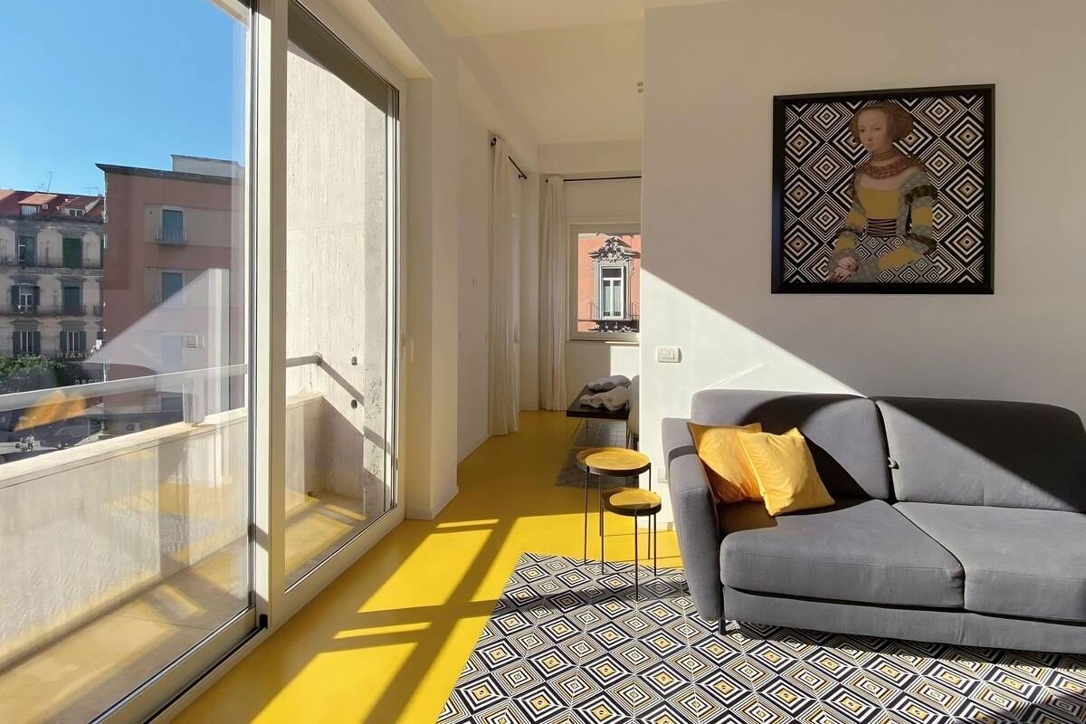 Un salon moderne avec un canapé gris, un tapis à motifs et une grande fenêtre donnant sur un paysage urbain.