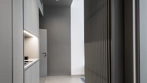 A modern hallway with a minimalist design, featuring a light-colored floor, a dark wall with a vertical panel, and a door at the end. - Toraldo Suites (Naples)