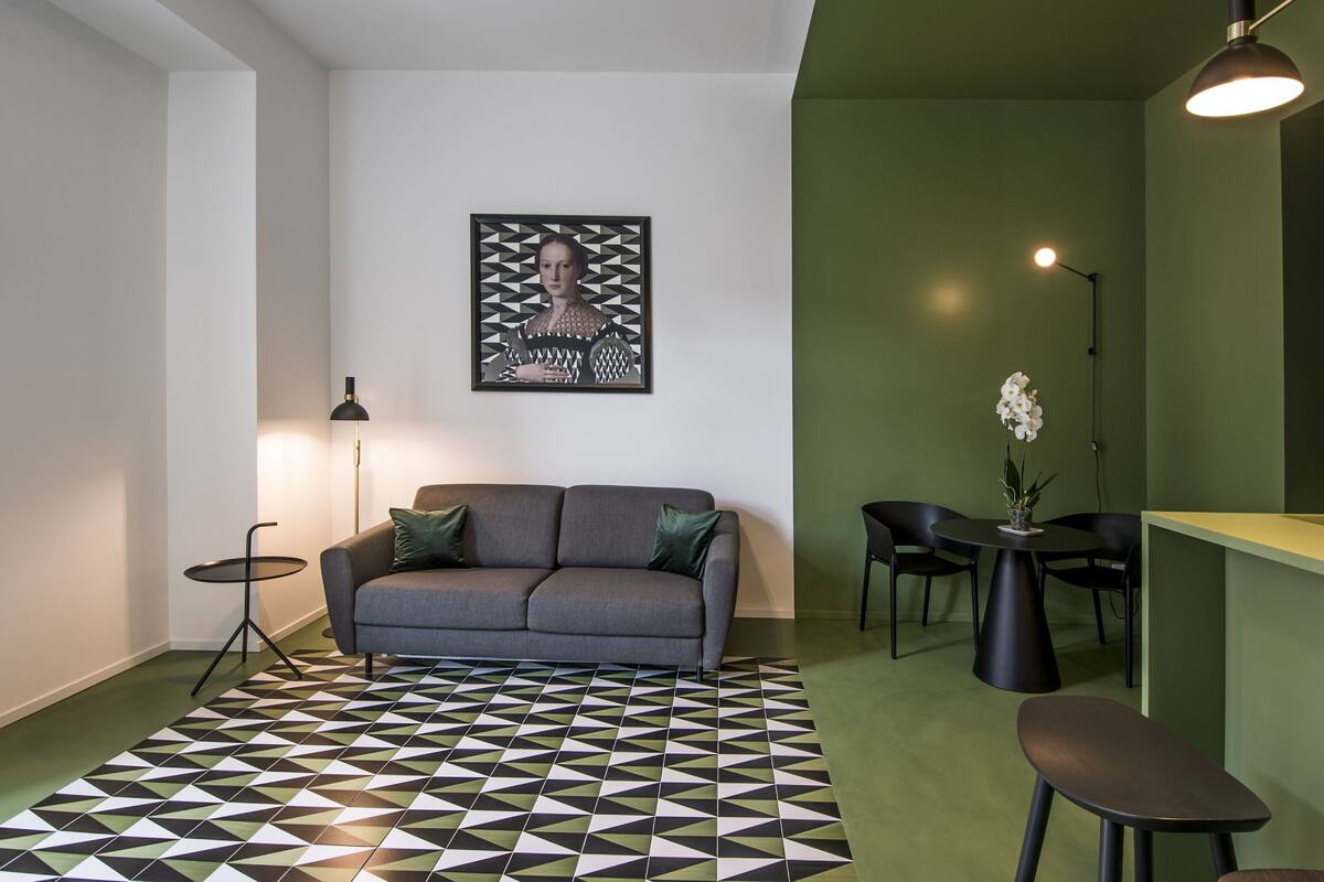 Un salon moderne avec un canapé gris, un tapis à motifs, un coin repas comprenant une table et des chaises, et un mur d’accent vert.