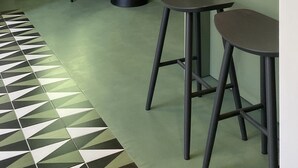 A modern interior with a green wall, a round table, two bar stools, and a floor lamp. - Toraldo Suites (Naples)