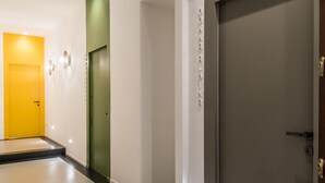 A modern hallway with a yellow door, a green door, and a large grey door. - Toraldo Suites (Naples)