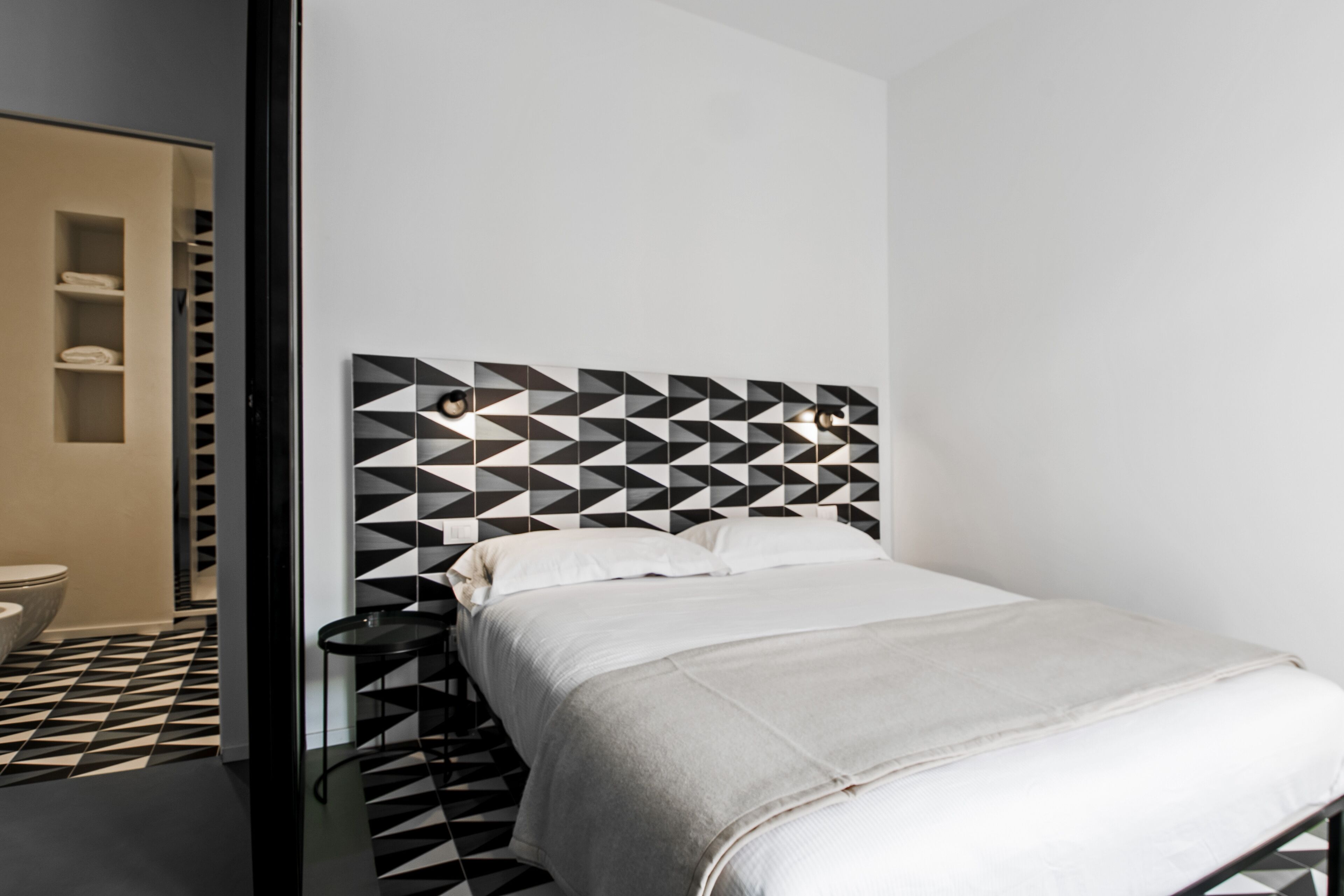 Un dormitorio moderno con una cabecera de diseño geométrico, una cama bien hecha y una mesita de noche pequeña.