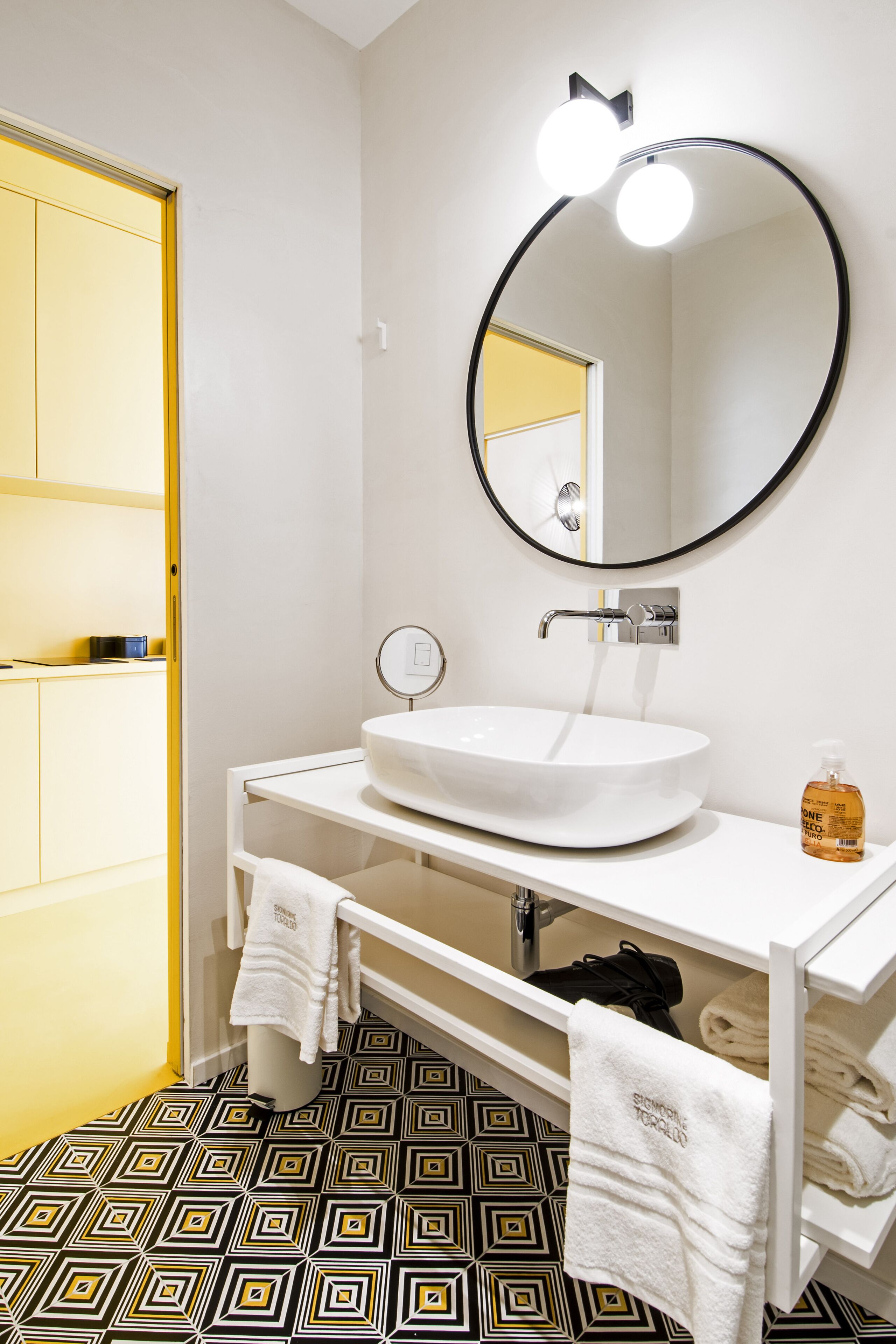Une salle de bain avec un lavabo blanc, un miroir rond et un carrelage décoré.