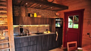 A compact kitchen with a stone wall backsplash, a red door, and a wooden chair. - Blockhaus Bodefall (Braunlage)