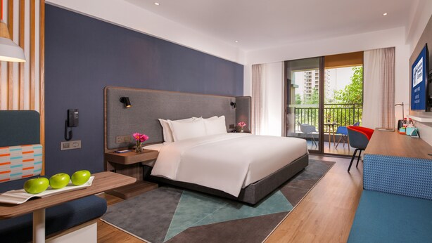 A modern hotel room with a large bed, a desk with a laptop, a chair, and a balcony with a view of the city. - Holiday Inn Express Chengdu East by IHG (Chengdu)