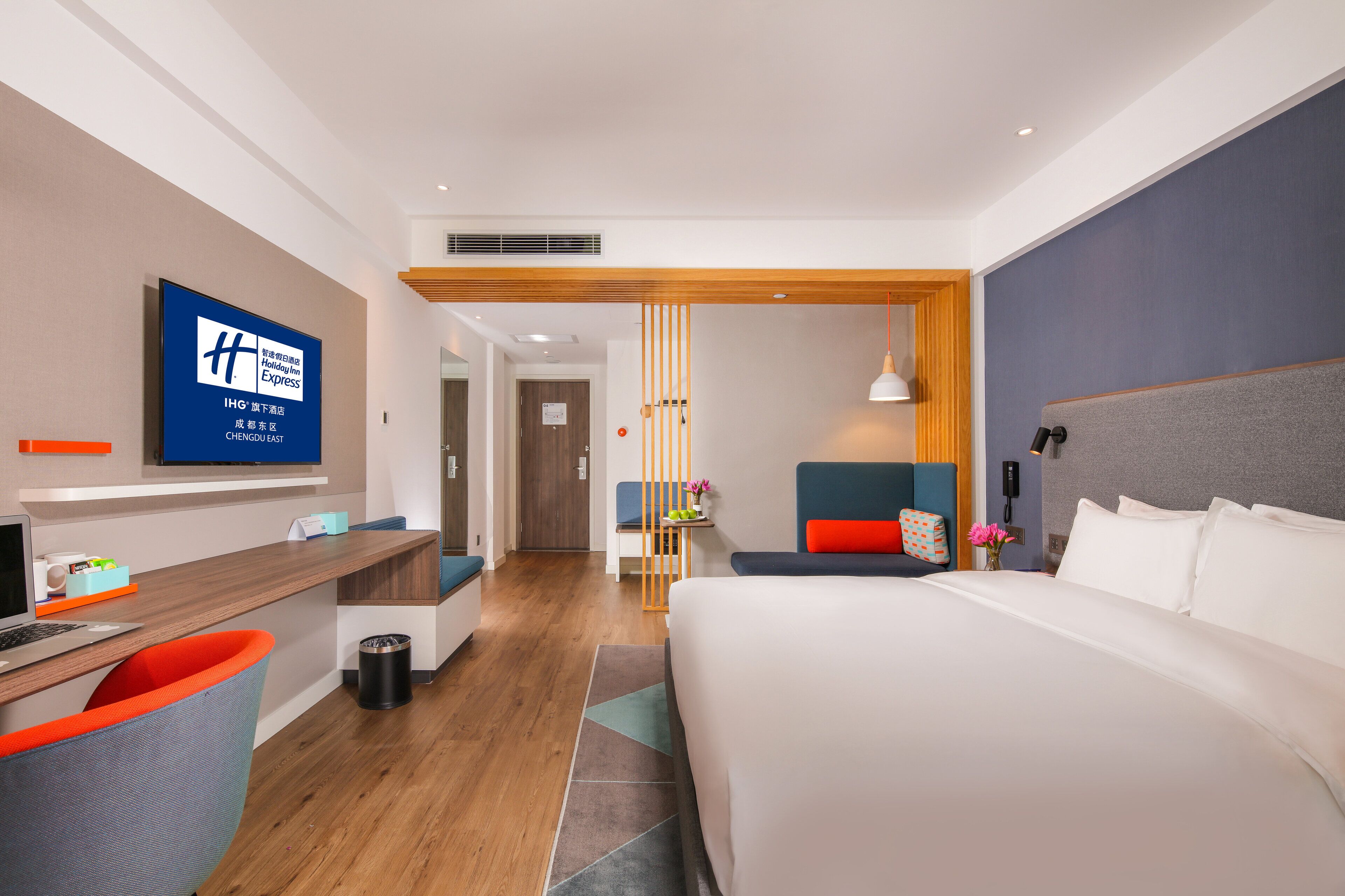 Una camera d'albergo moderna con un letto grande, una scrivania con un computer, una TV fissata al muro e un pannello divisorio in legno.