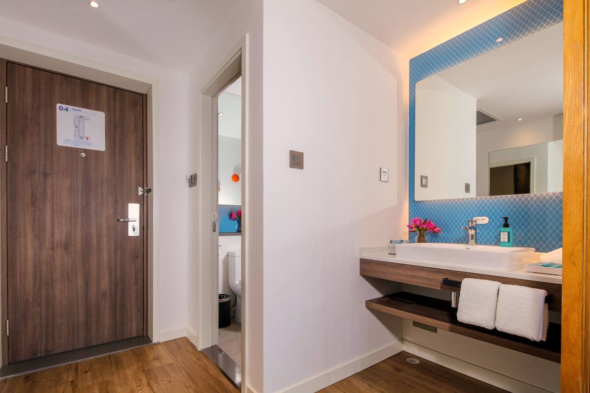 A modern bathroom with a wooden door, a sink with a mirror, and a blue tiled wall.