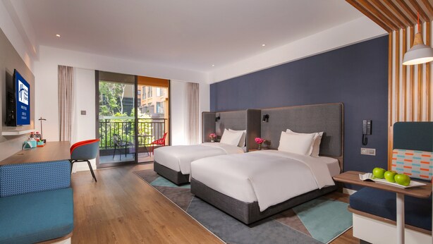Habitación de hotel moderna con dos camas, un escritorio, un televisor y un balcón con vistas a zonas verdes.