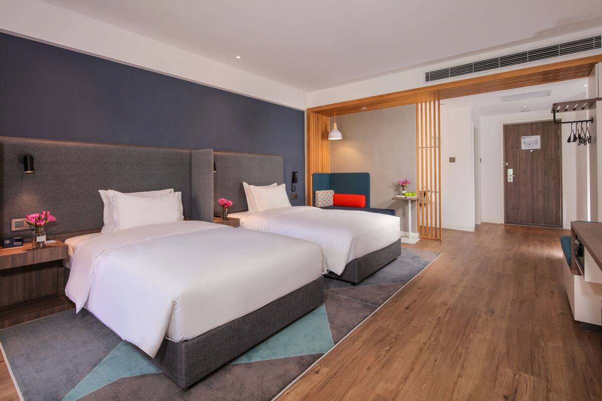 A modern hotel room with two beds, a wooden floor, and a large mirror.