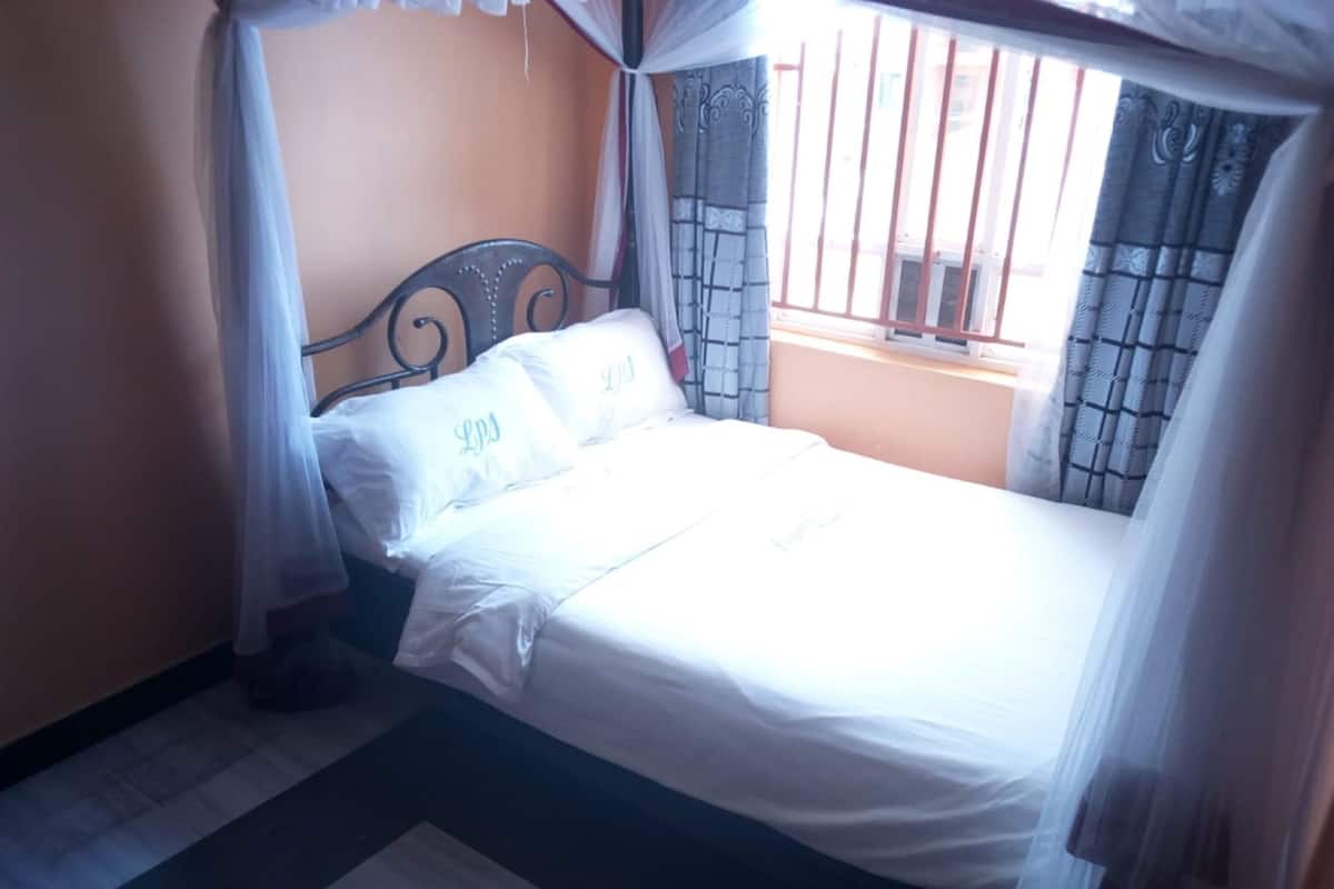 A bed with white linens and a metal headboard, a window with bars, and a curtain.