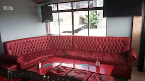 Ein rotes Ledersofa mit passendem Sessel und einem kleinen Tisch in einem Zimmer mit großen Fenstern und einem Lautsprecher an der Wand.
