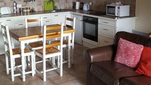 Une cuisine moderne avec des meubles blancs, une table à manger en bois et un canapé en cuir marron.