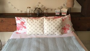 Un lit bien fait, recouvert d’une couvre-lit à motifs, avec deux oreillers ornés de motifs floraux, et un mur décoré de motifs en forme de cœur et de deux citations inspirantes.