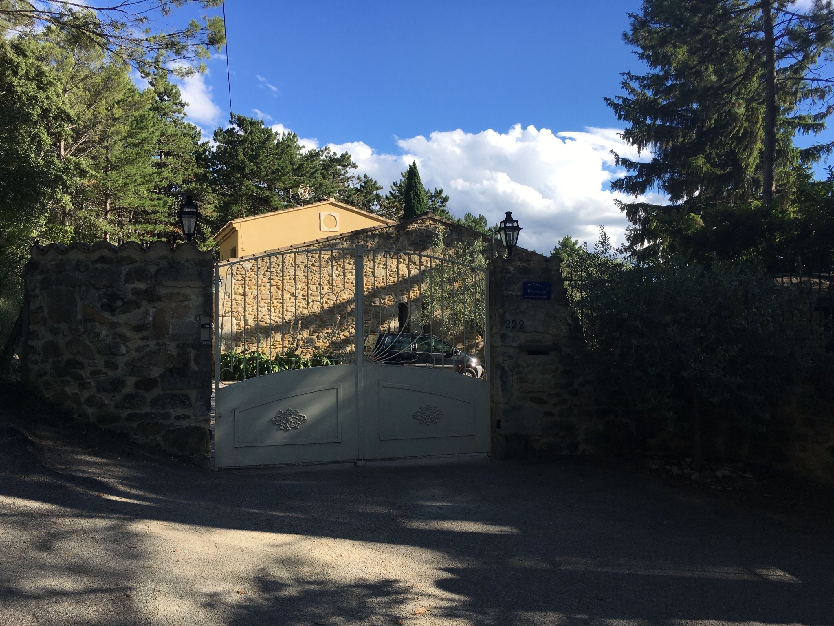 A gated entrance with a stone wall, a metal gate, and a building with a sign.