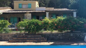 Un edificio de dos pisos con fachada de piedra, contraventanas verdes y techo de tejas.