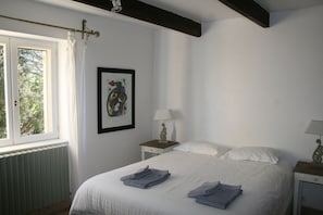 Un dormitorio con cama, dos mesitas de noche, una ventana con cortinas, un radiador y un cuadro enmarcado en la pared.