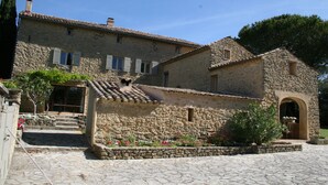 Un edificio de piedra con un patio, escalones que llevan a la entrada y un pequeño jardín con flores.