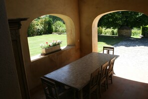 Un patio con mesa y sillas, una jardinera llena de flores y vistas a un jardín a través de un arco.